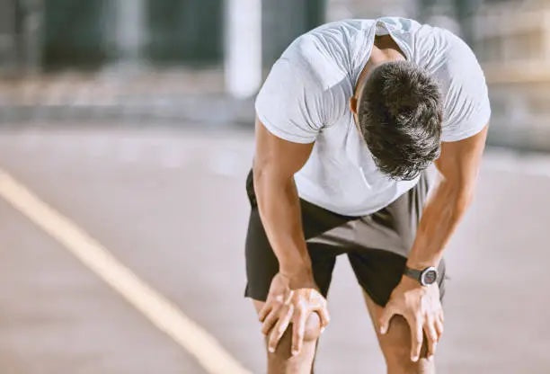 Image of a person in work-out clothing, hands on knees, resting after exercise