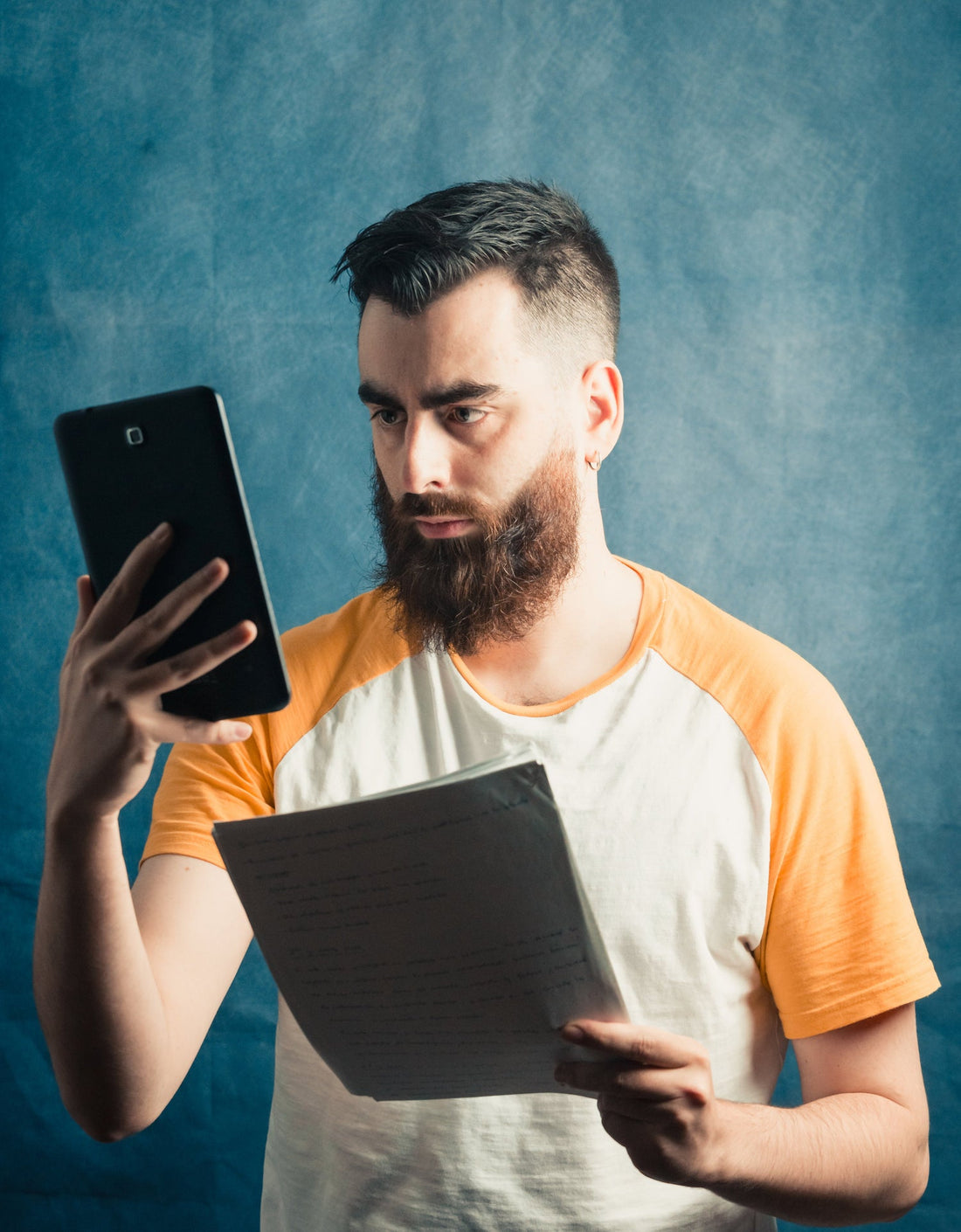 Image of a male staring at an electronic tablet while holding bunch of papers in other hand. Concentration. 