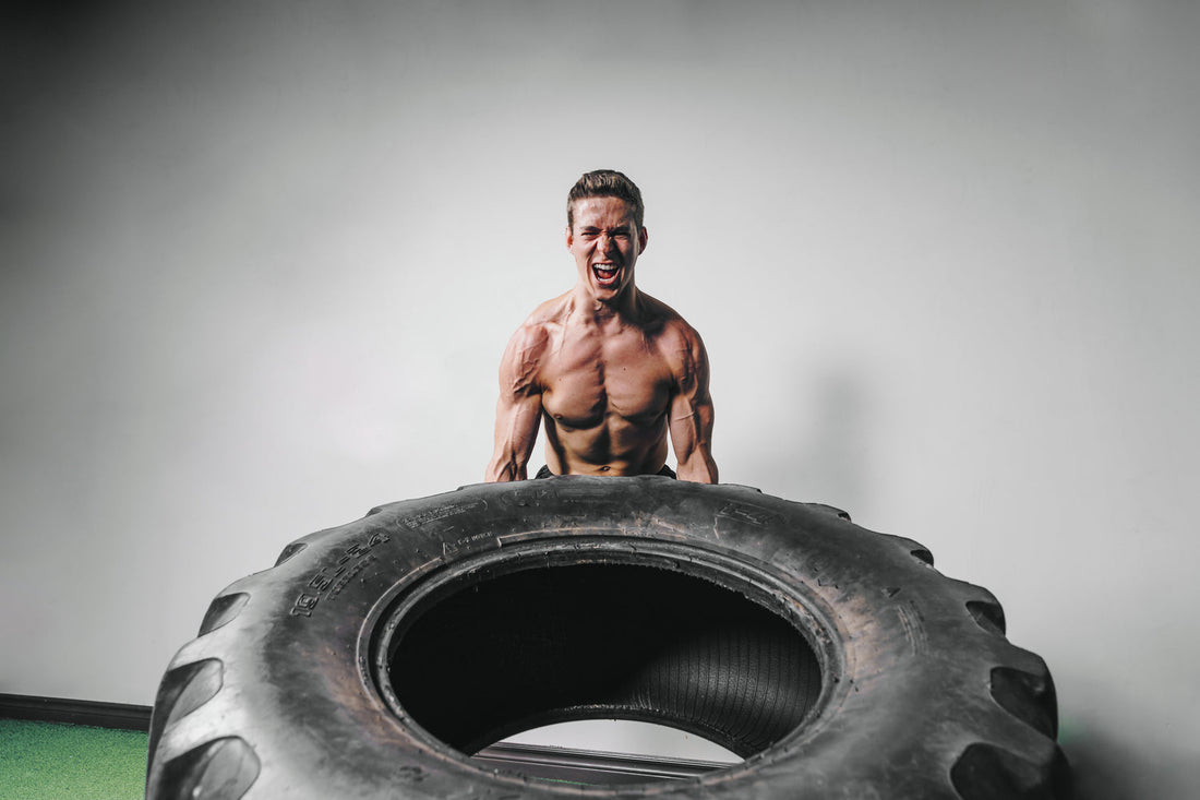 Image of male without a shirt lifting a very large tire. Lots of muscles. 