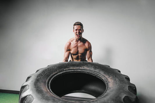 Image of male without a shirt lifting a very large tire. Lots of muscles. 