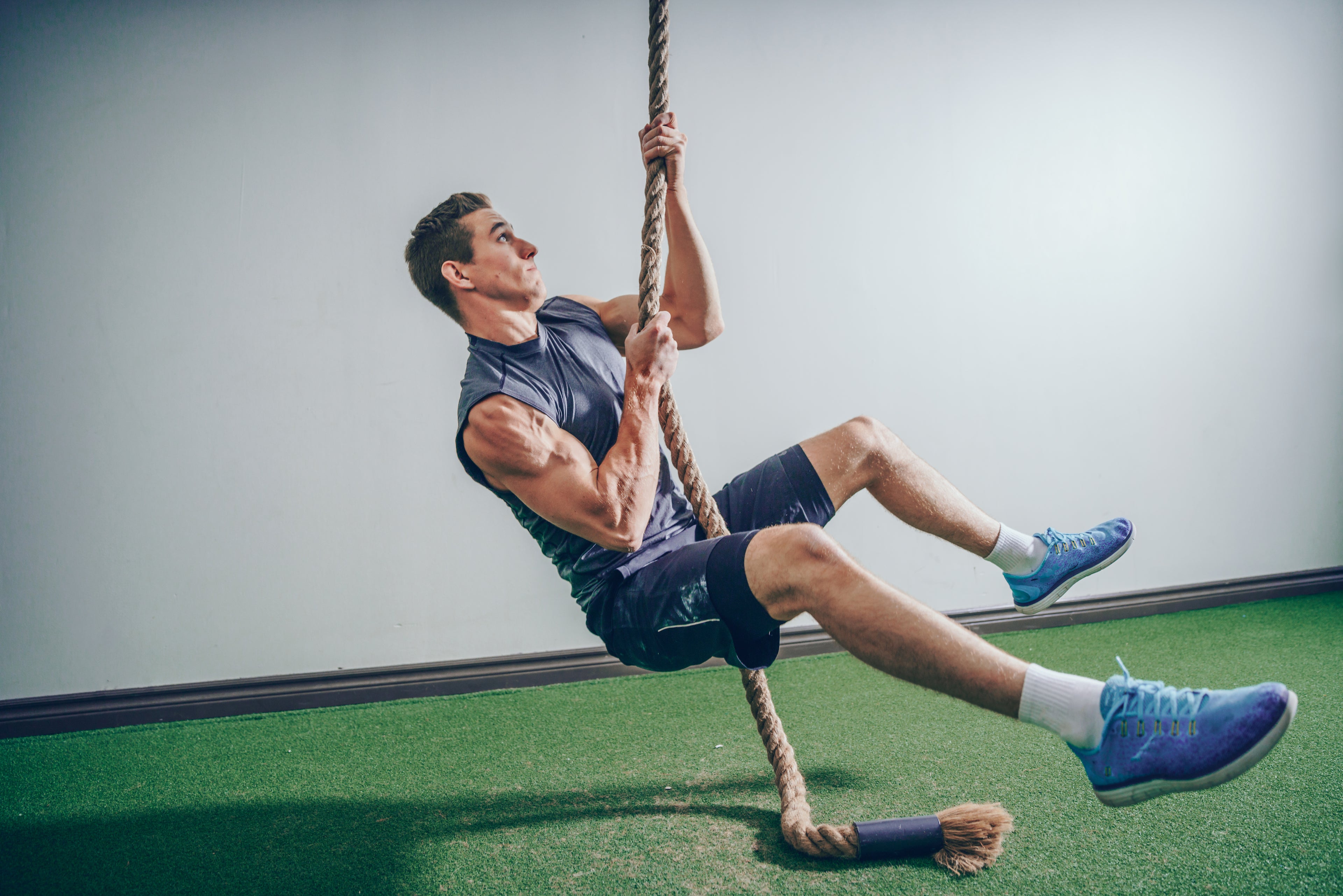 Fit man in gym setting climbing a rope. Muscles, fitness, strength. Male in 20s-30s. 